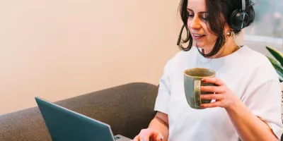 Vrouw in zetel met laptop op de schoot en een koffie in de hand