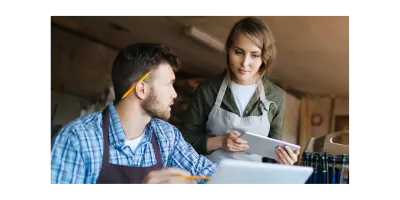 Twee werknemers in een middelgroot bedrijf gebruiken HR-software op laptop en tablet voor personeelsbeheer en tijdregistratie.