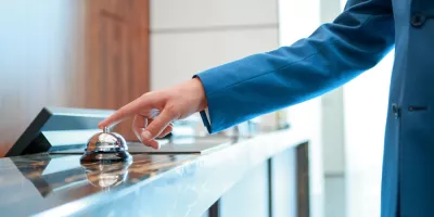 Person in a blue coat pressing a service bell at a reception desk