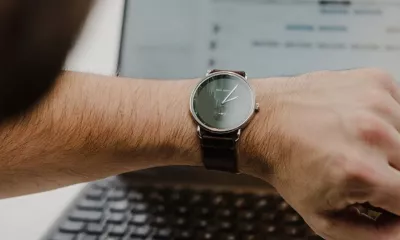 Employee checking a wristwatch while working on a laptop, illustrating Protime time and attendance tracking and time registration