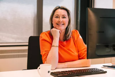 Vrouw aan bureau achter computer kijkt in de camera