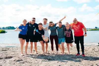 Acht collega's in sportkleding lachen en poseren samen op een zonnig strand