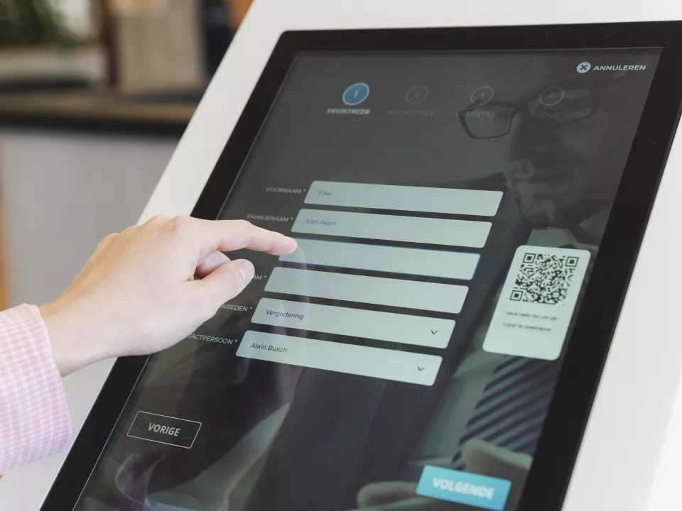 Een bezoeker registreert zich op een touchscreen kiosk bij de ingang van een gebouw
