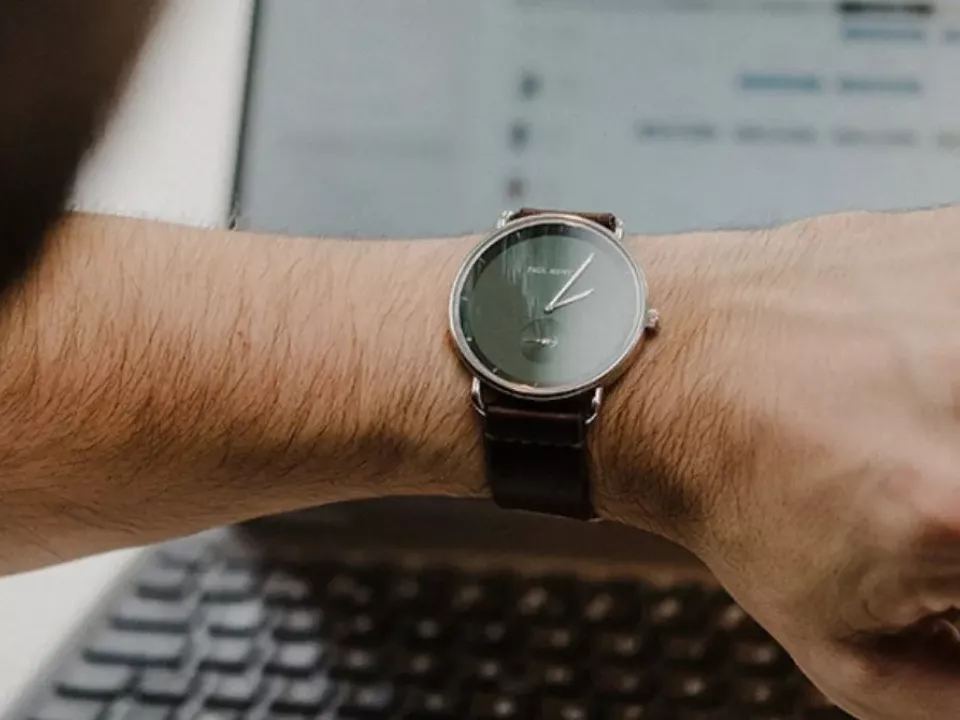 Employee checking a wristwatch while working on a laptop, illustrating Protime time and attendance tracking and time registration