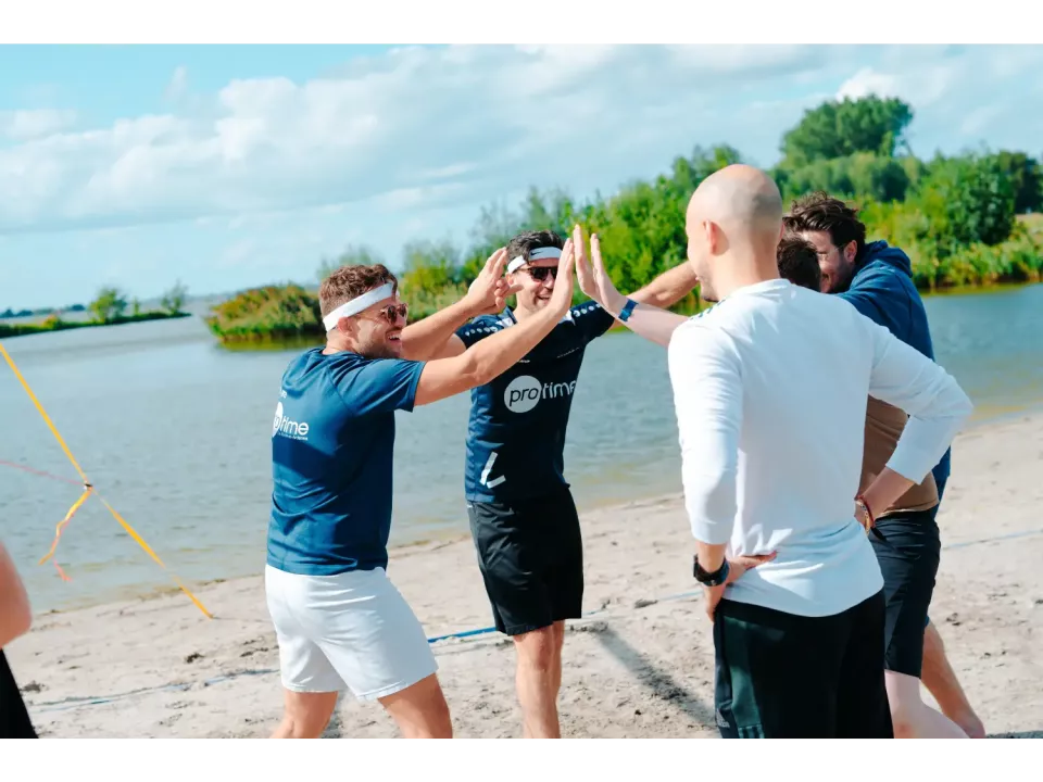 Groep collega's op een strand viert feest met high-fives bij het water.