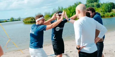 Groep collega's op een strand viert feest met high-fives bij het water.